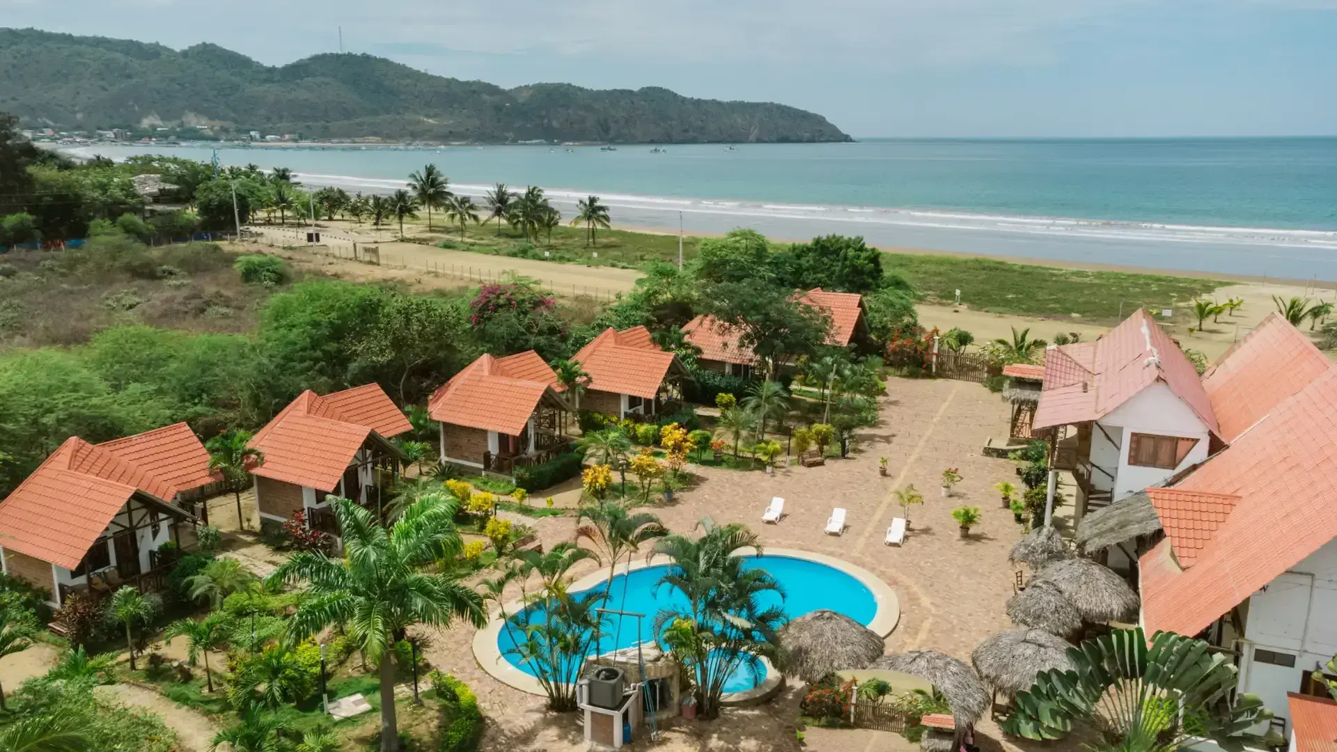 Aerial view of Oceanic Hostería — tile-roofed cabins, a blue pool and tropical gardens facing the Pacific in Puerto López, Manabí, Ecuador